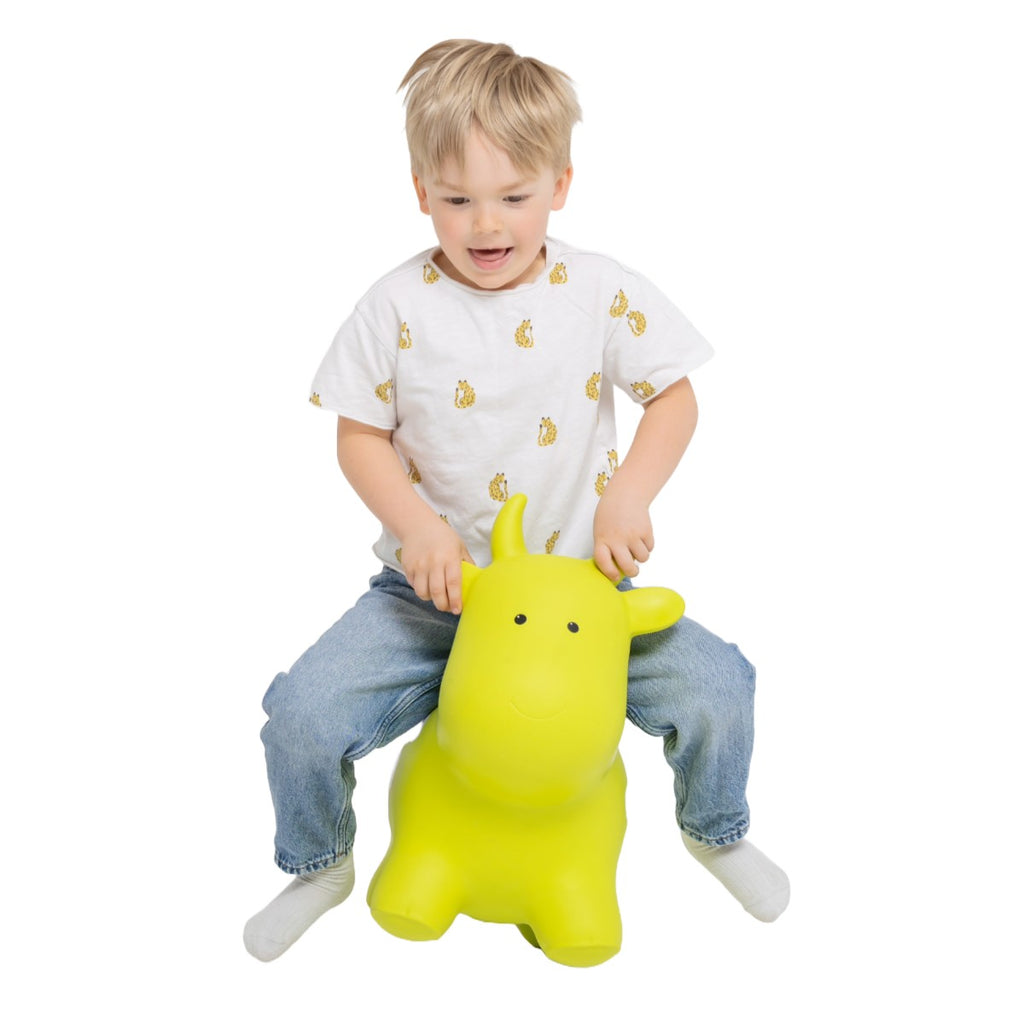 a joyful toddler bouncing on a green cow hopper toy in a sunlit garden