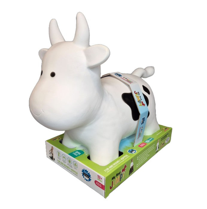 a smiling toddler bouncing on a white cow hopper toy in a sunny garden