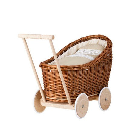 a soft-focus side view of the natural wicker doll pram with cozy beige bedding in a sunlit nursery