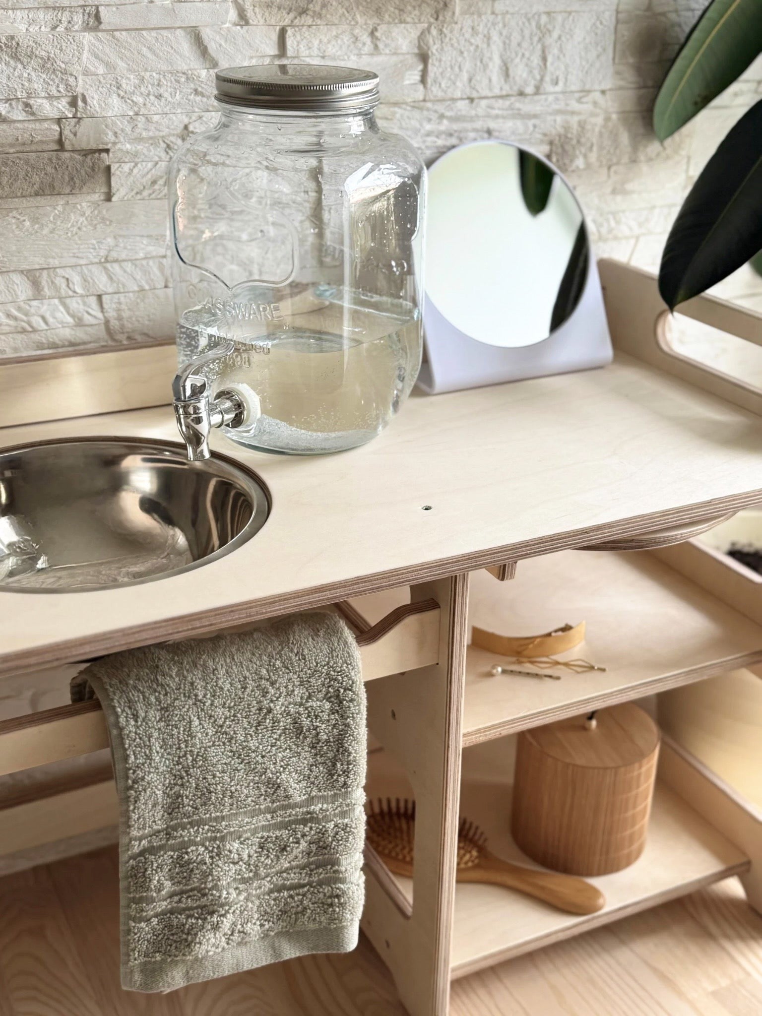 a toddler giggling as they wash hands at their own wooden montessori sink