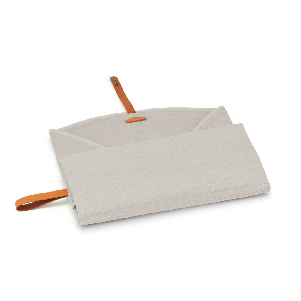 a soft beige dog travel mat with a leather belt, laid out on a cozy carpet