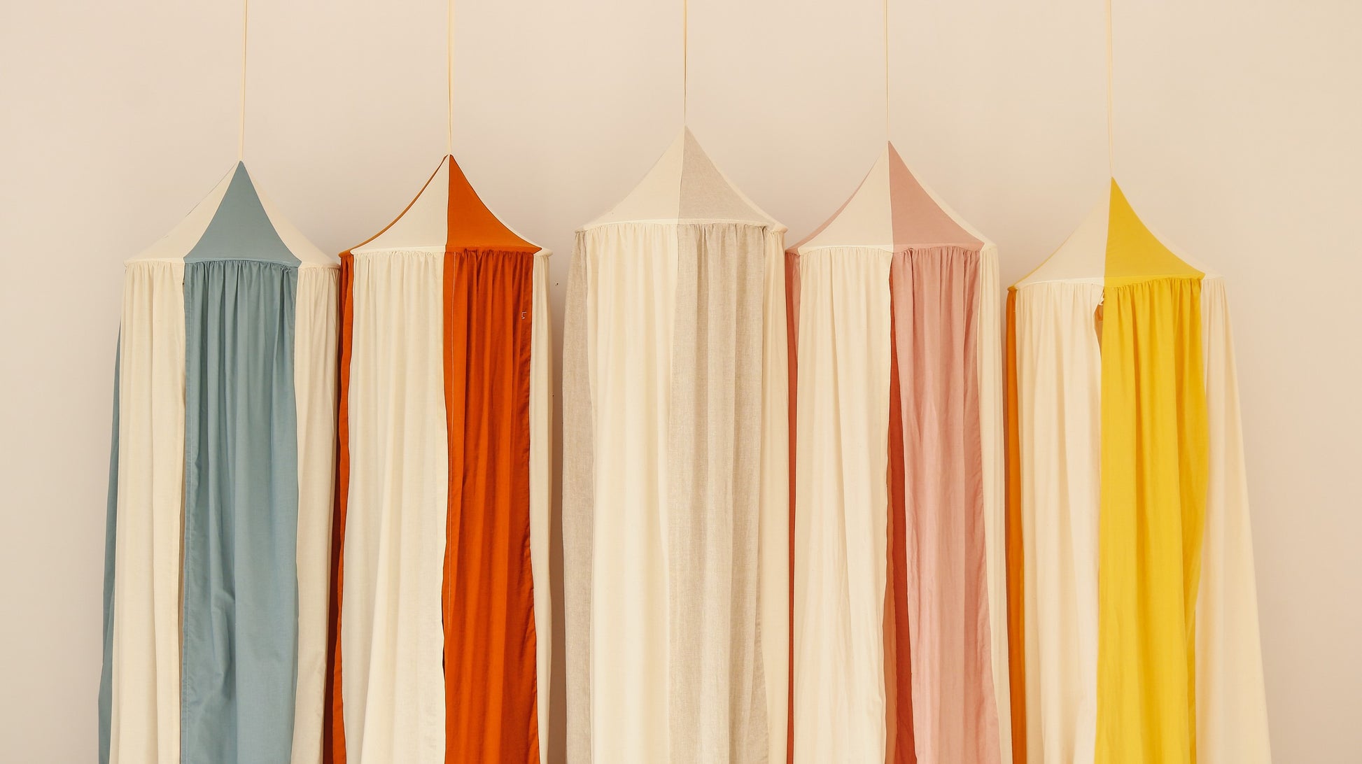 powder pink kids play canopy with soft toys hanging inside in a sunlit room
