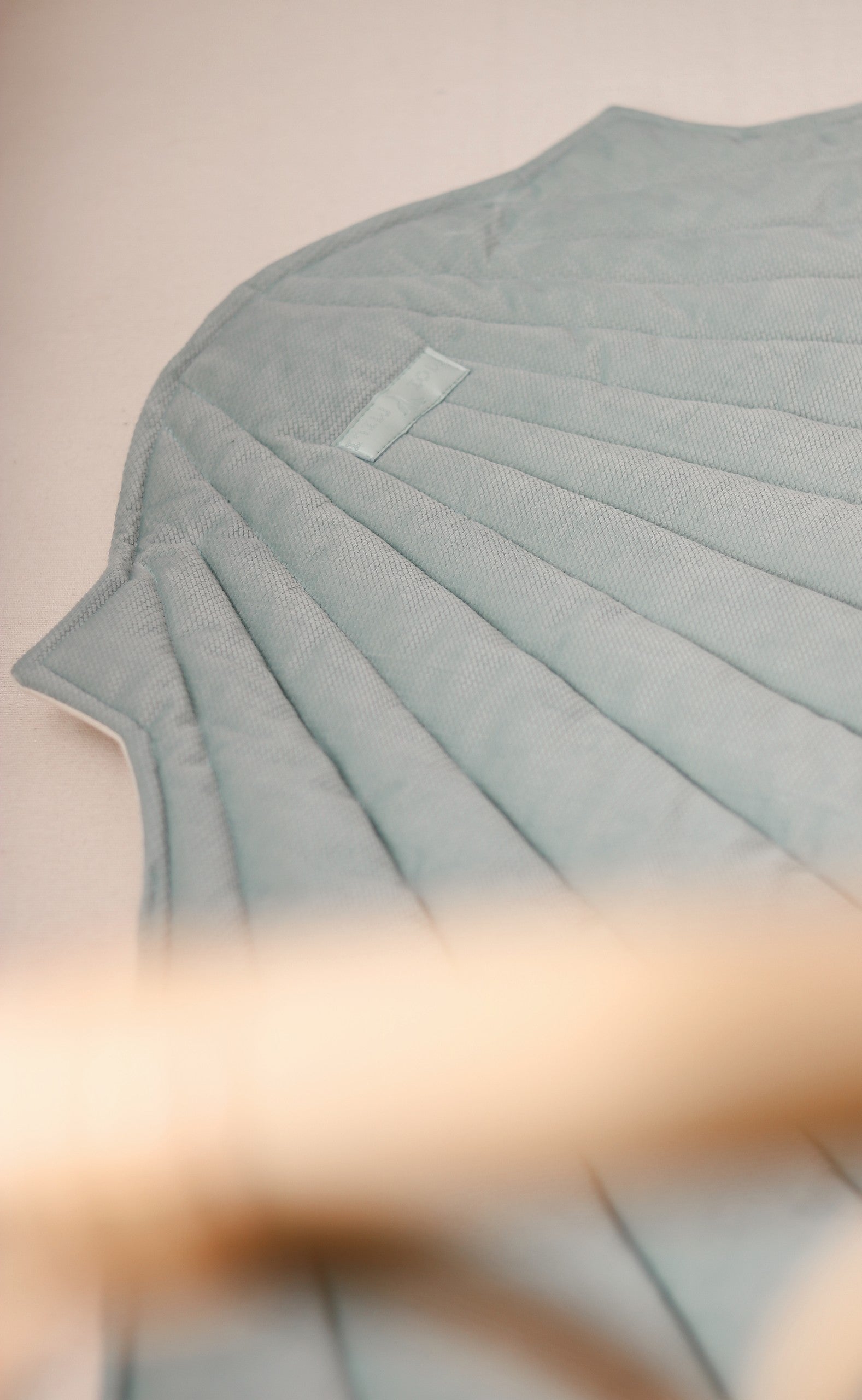 mint green organic cotton and velvet playmat laid flat on grass, showcasing its ginkgo leaf shape and practical double-sided design