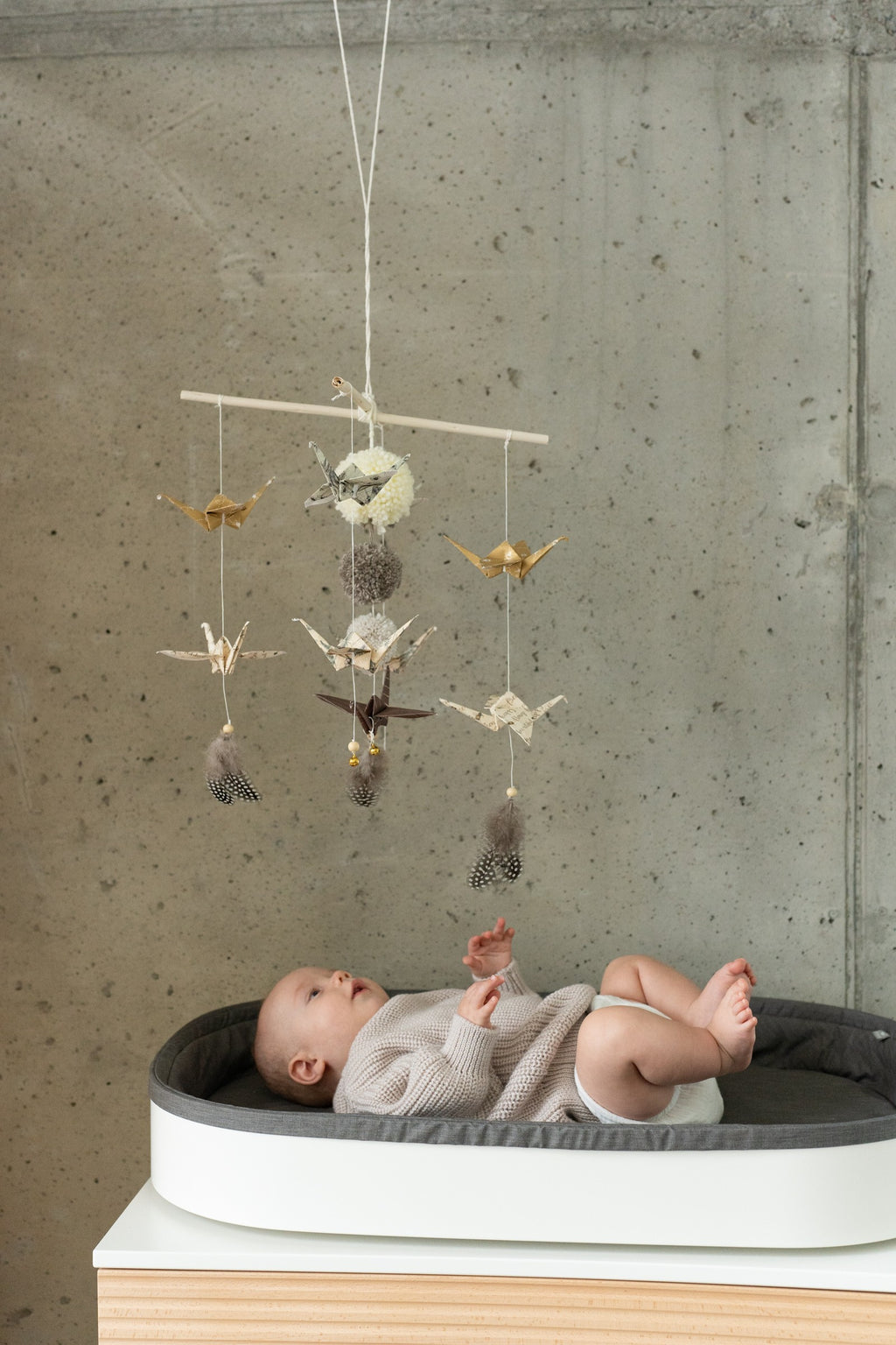 gold dust origami nursery mobile hanging above crib with delicate paper cranes and pompoms in soft light