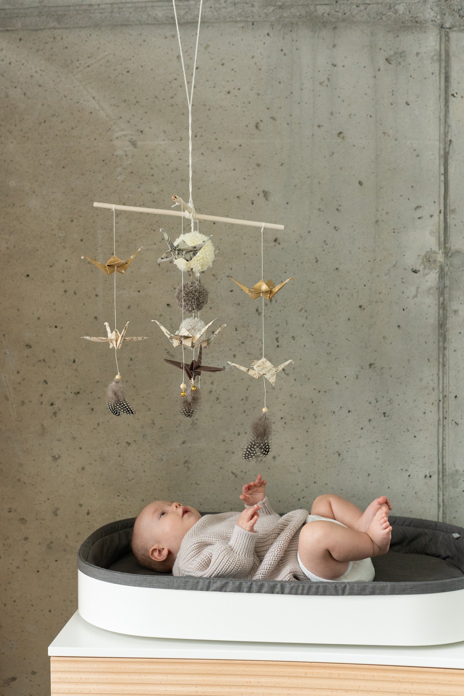 gold dust origami nursery mobile hanging above crib with delicate paper cranes and pompoms in soft light