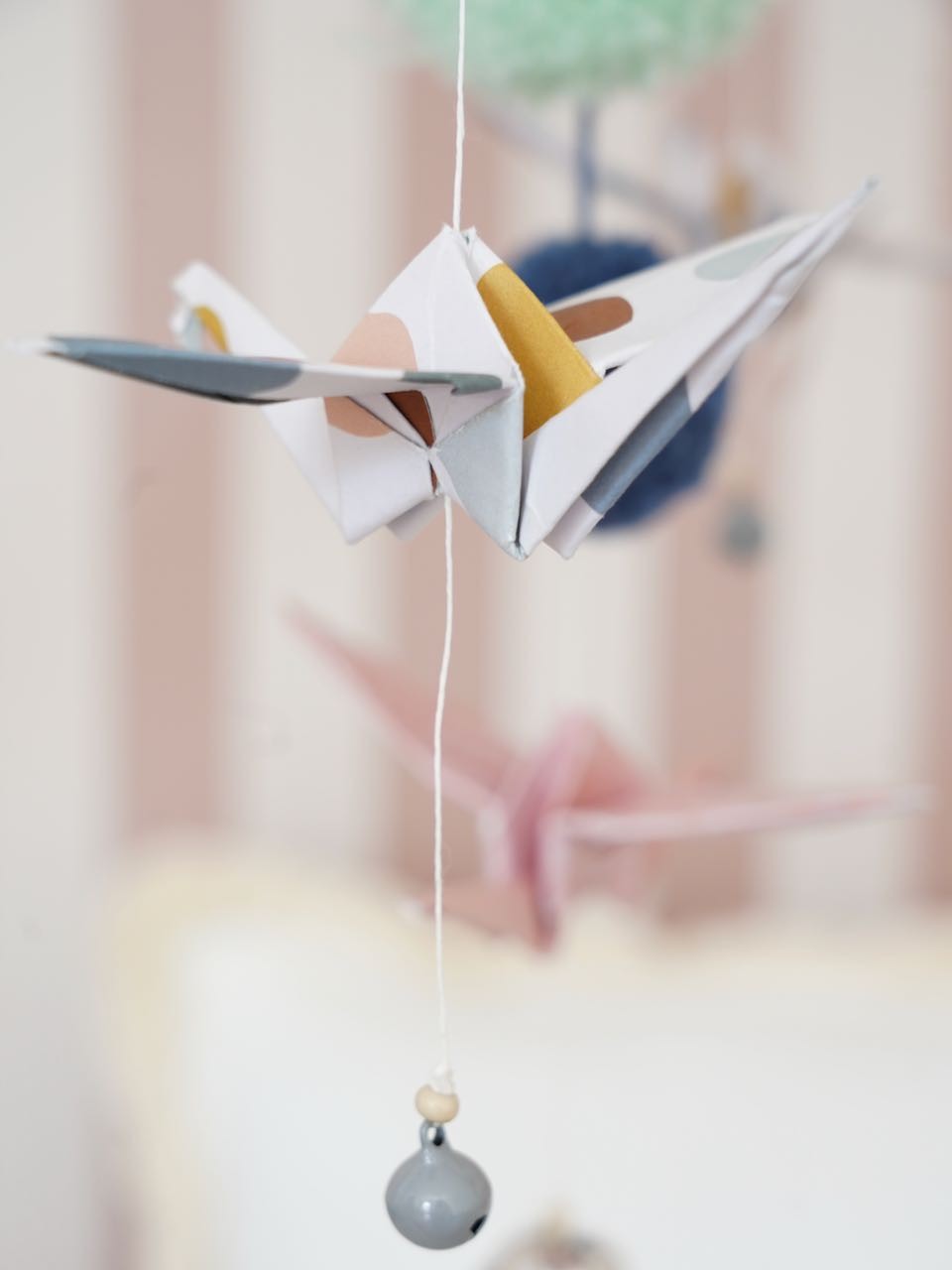 elegant pastel origami mobile with delicate cranes and pompoms, softly lit in a serene nursery setting