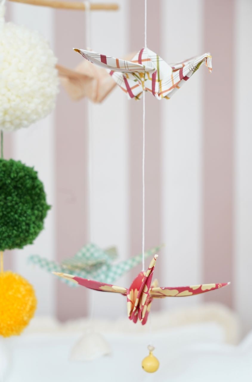 soft morning light on a handcrafted origami mobile with paper cranes and yarn pompoms