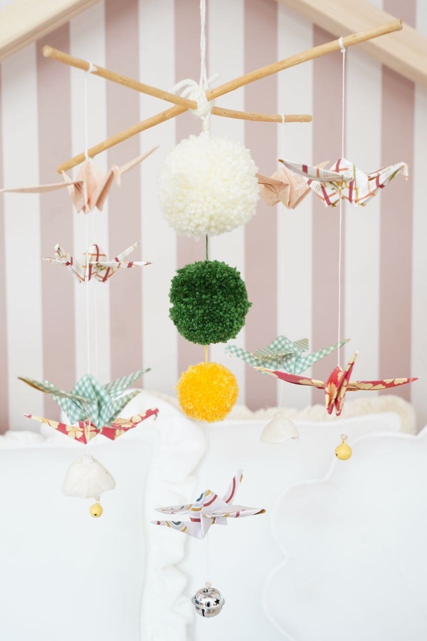 bold handcrafted origami mobile with vibrant pompoms and wooden sticks for a nursery