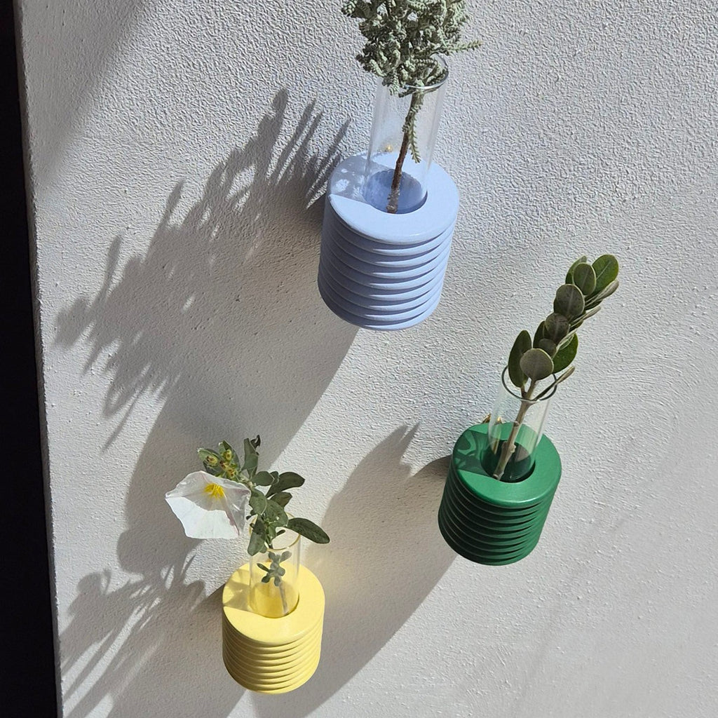 playful light blue ribble wall vase with a single cheerful wildflower on a sunny yellow background