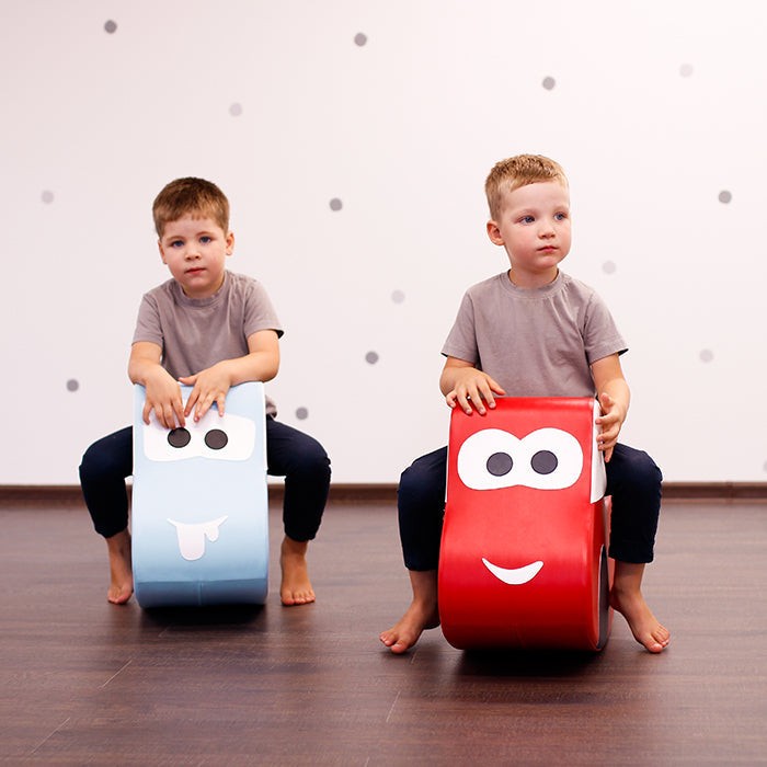 smiling toddler zooming on a bright red soft play car, giggling with hands on the wheel