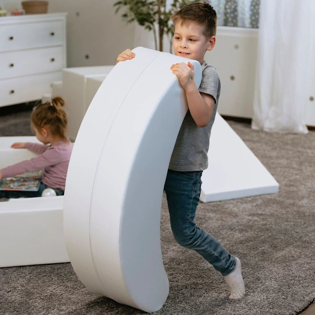 smiling toddler rocking on soft white banana toy in sunny playroom, boosting balance and giggles