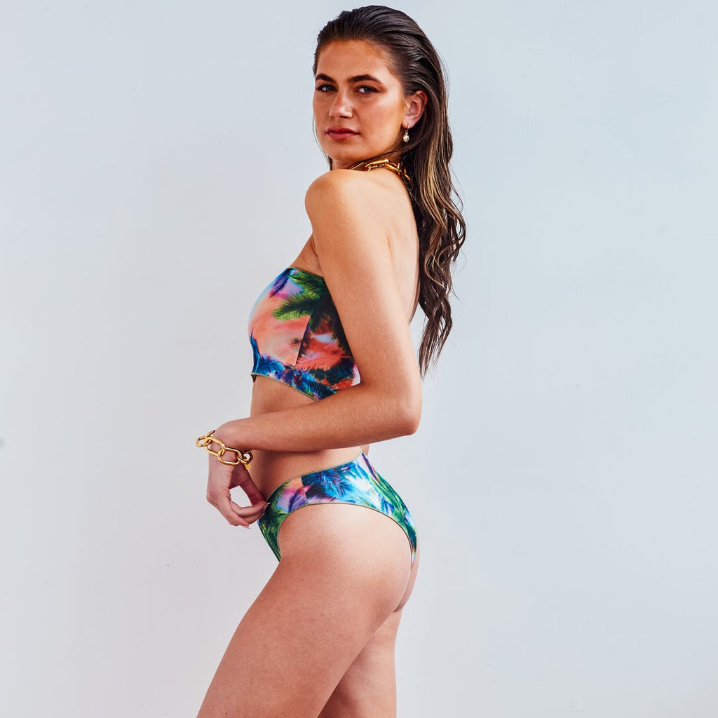 soft electric palm bikini set draped on sandy shore, bandeau style with gentle sunlight highlighting tan-through fabric