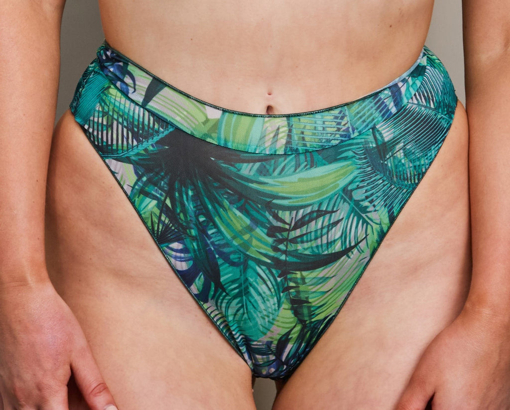 soft tropical palm green bikini set draped on a sunlit beach towel, showcasing its tan-through fabric and adjustable seashell style