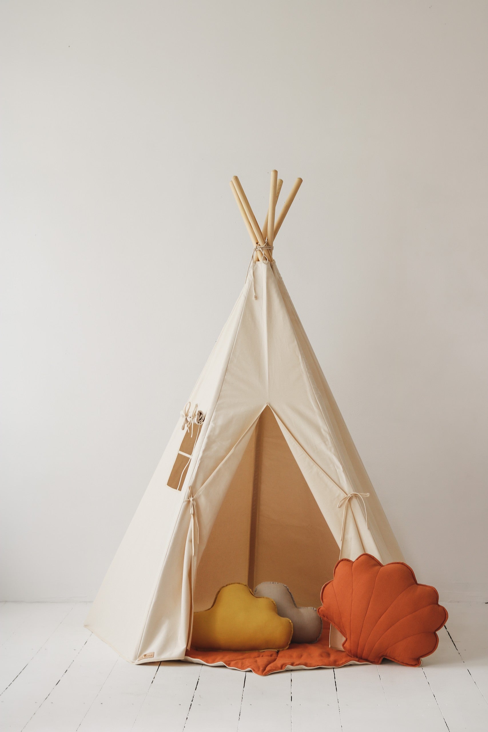 soft beige teepee tent for kids with cozy cotton fabric and pine poles, set up in a sunny playroom corner
