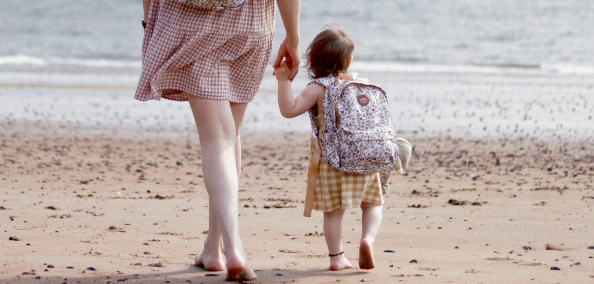 Woman and child walking on a beach with patterned backpacks. Modern cloth Nappies brand at Sostter