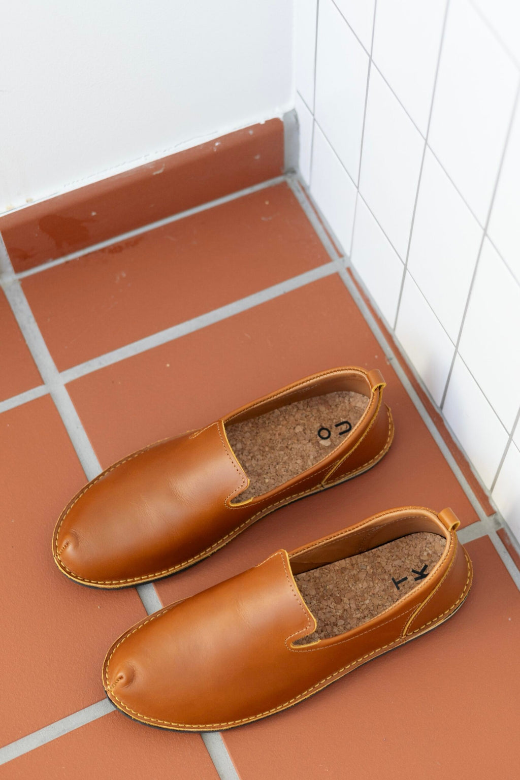 elegant ocre leather loafers with cork insole, side profile on marble surface, soft lighting highlighting craftsmanship