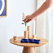 playful medium totem vase with a single bright flower in its glass insert on a sunlit table