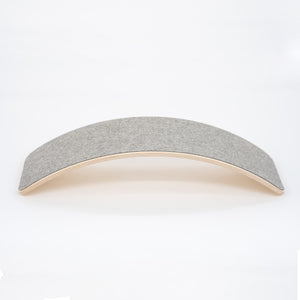 a child gently rocking on a wooden balance board with soft grey felt in a cozy, sunlit room