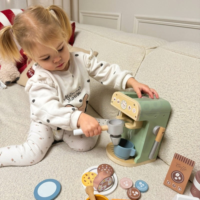 a child's hand placing a wooden pastry on a saucer beside the woopie green coffee maker
