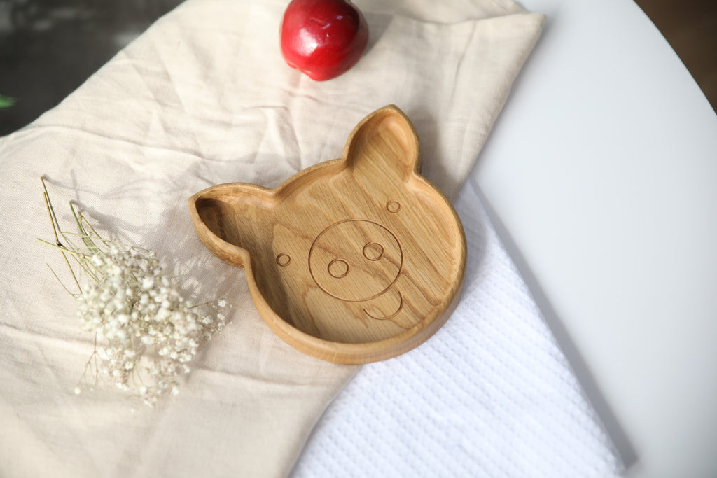 soft-lit wooden pig plate for kids with smooth hand-polished surface, resting on a cozy kitchen table